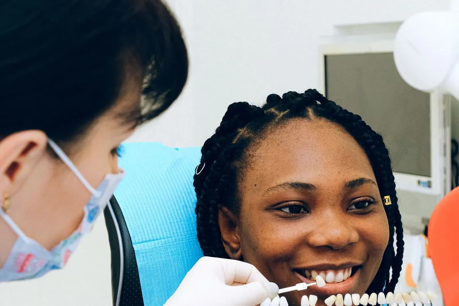 Dentist matching a tooth shade guide against a smiling patient's front teeth before veneers