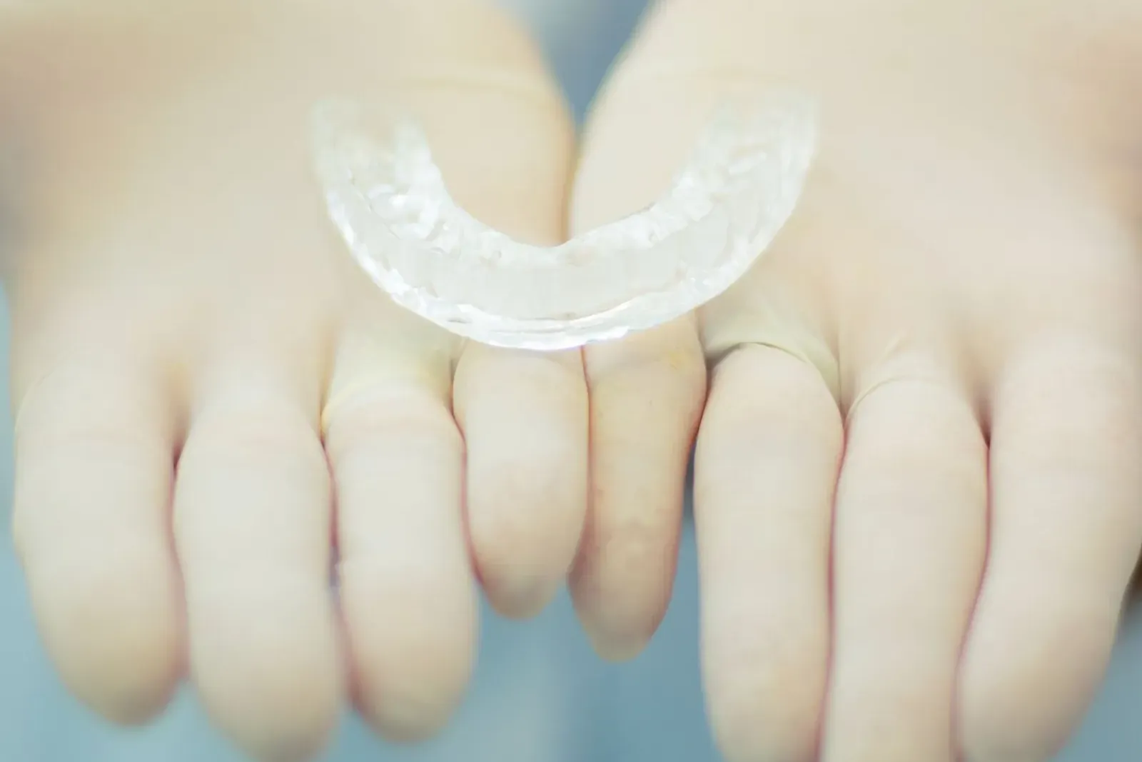 Clear custom-made night guard for teeth grinding, held in a pair of hands